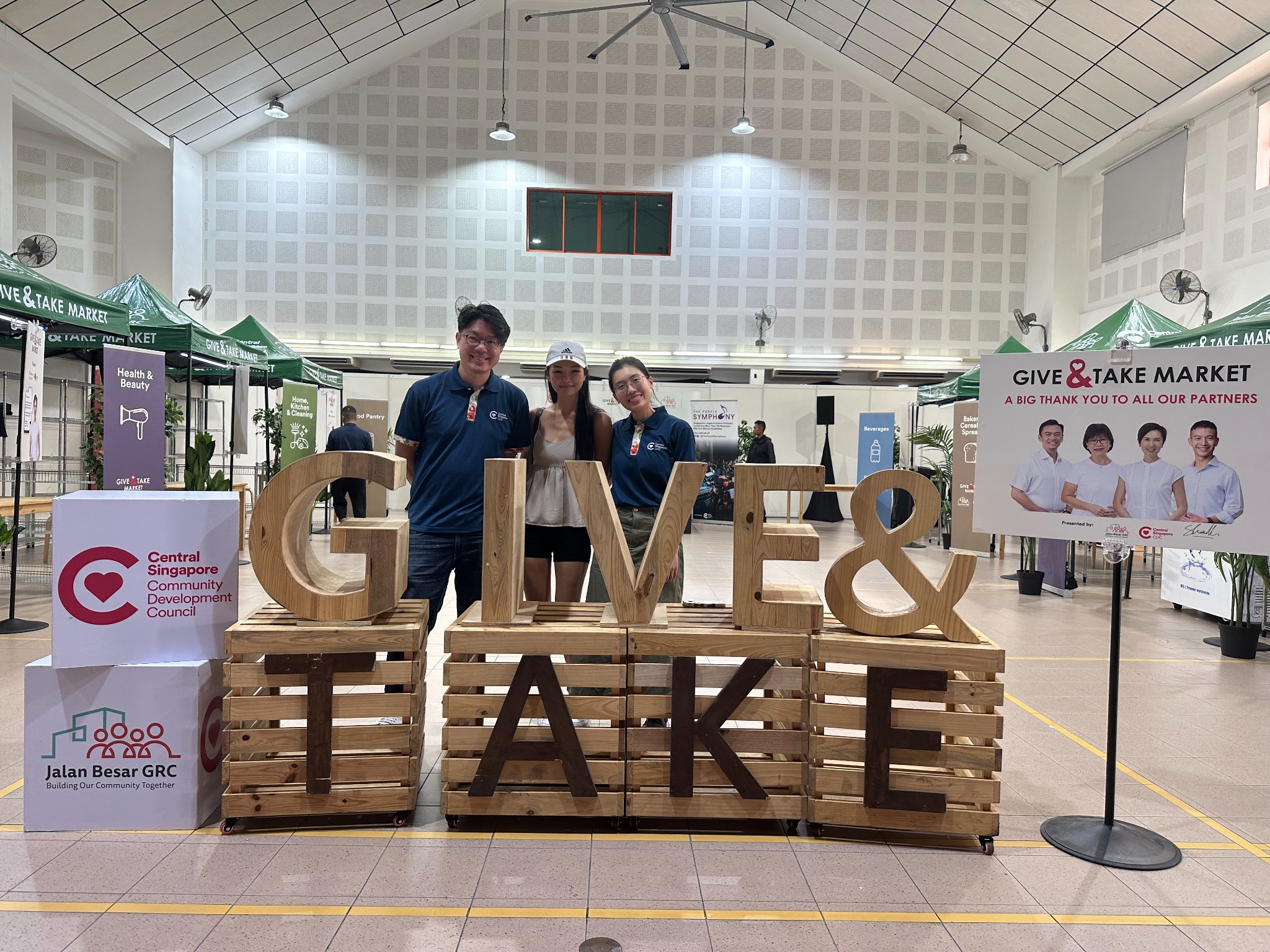 Three attendees together beside the Give & Take Market display at Geylang West CC